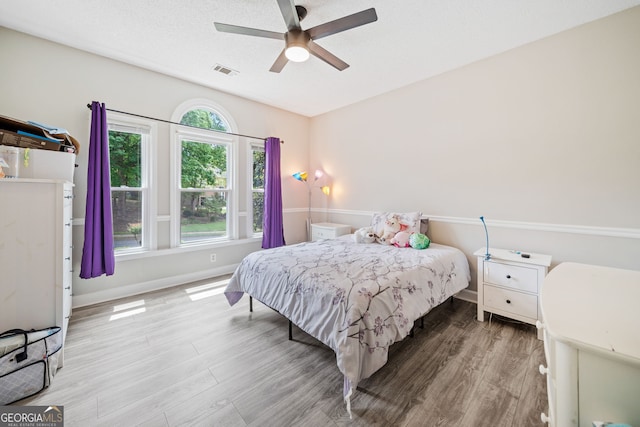 bedroom with a ceiling fan, baseboards, visible vents, and wood finished floors