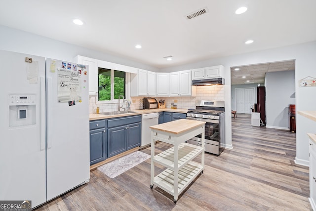kitchen featuring blue cabinets, visible vents, light wood-type flooring, a sink, and white appliances