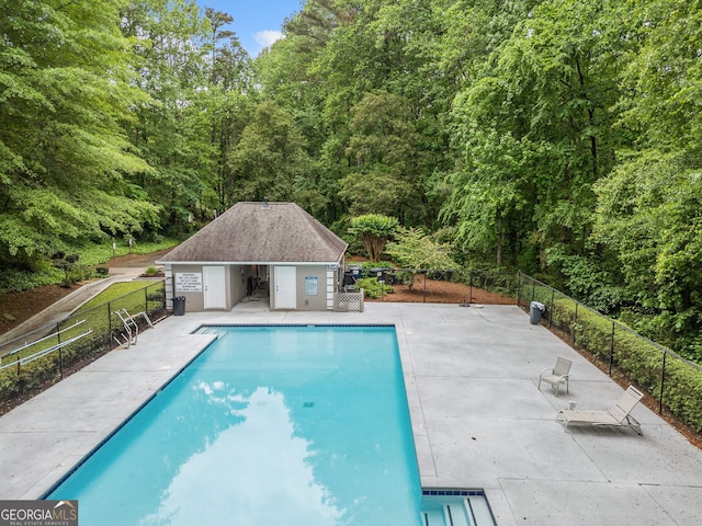 pool featuring a patio, fence, and a wooded view