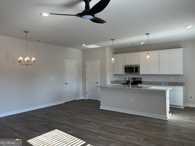 kitchen with dark wood finished floors, a sink, stainless steel microwave, ceiling fan with notable chandelier, and white cabinetry