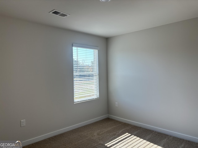 empty room with baseboards, visible vents, and dark colored carpet