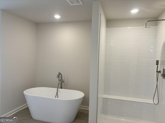 bathroom with baseboards, wood finished floors, a tile shower, and a soaking tub