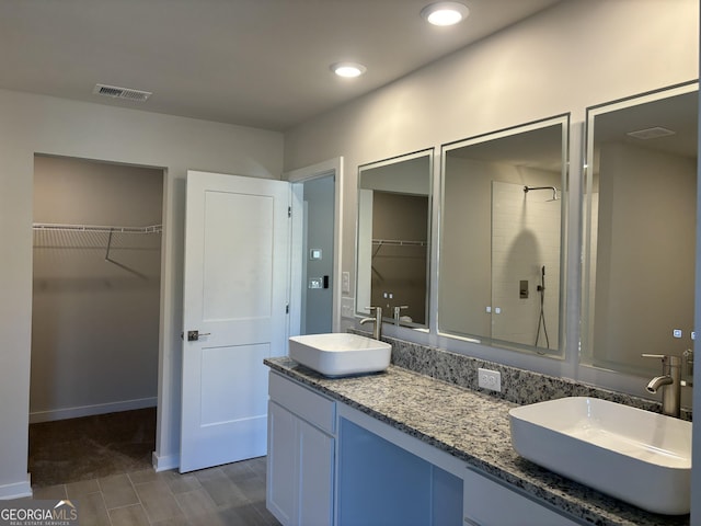 bathroom with a sink, a walk in closet, a tile shower, and visible vents