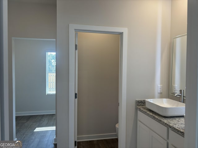 bathroom featuring toilet, baseboards, wood finished floors, and vanity