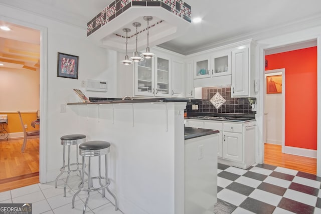 kitchen with white cabinets, dark countertops, a breakfast bar area, backsplash, and glass insert cabinets