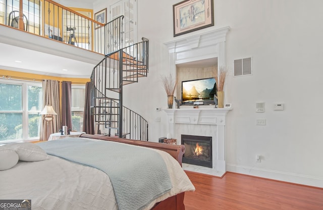 bedroom with visible vents, a glass covered fireplace, wood finished floors, baseboards, and a high ceiling