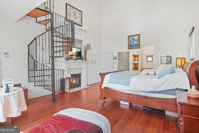 bedroom featuring baseboards, ornamental molding, a towering ceiling, and wood finished floors