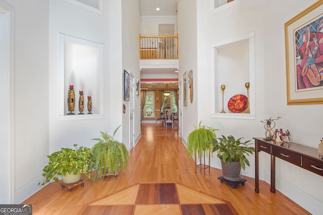 hall with baseboards, a high ceiling, ornamental molding, and wood finished floors