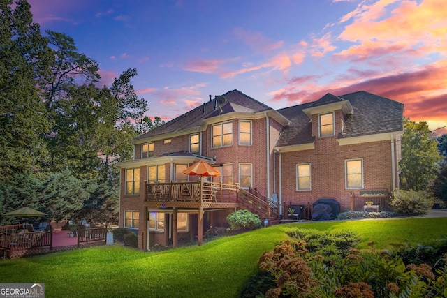 rear view of property featuring a yard, a deck, and brick siding
