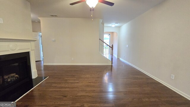 unfurnished living room featuring ceiling fan, visible vents, arched walkways, dark wood-style floors, and a glass covered fireplace