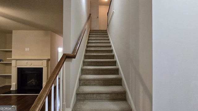 stairway featuring baseboards, a fireplace with raised hearth, and a towering ceiling