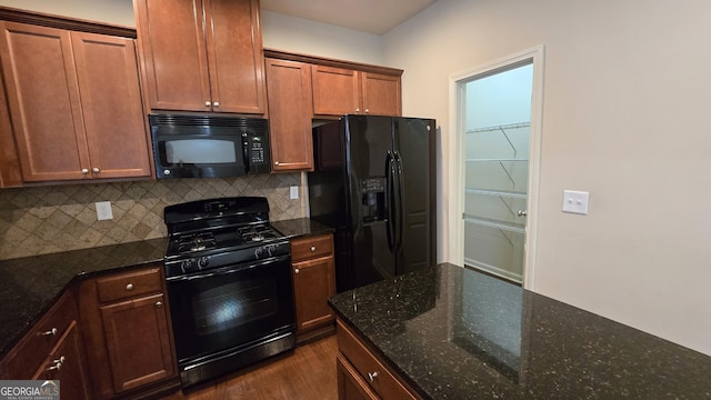 kitchen featuring dark wood-type flooring, dark stone counters, black appliances, and tasteful backsplash
