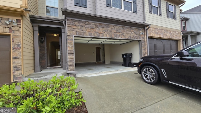 doorway to property with an attached garage, concrete driveway, and stone siding