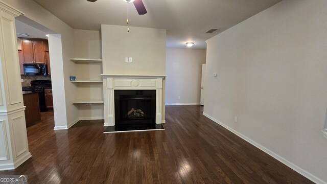 unfurnished living room with visible vents, baseboards, dark wood-type flooring, a fireplace with raised hearth, and a ceiling fan