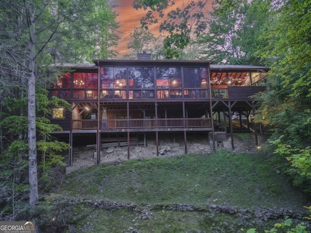 rear view of house with a sunroom, a wooden deck, and a chimney