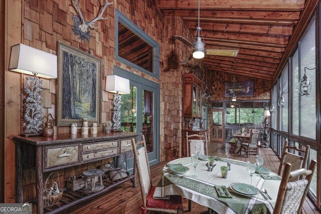dining room featuring wood-type flooring, a ceiling fan, lofted ceiling with beams, and wooden walls