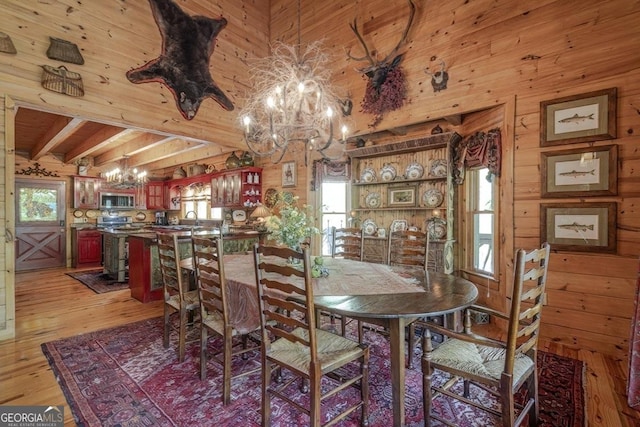 dining area featuring wooden walls, beamed ceiling, light wood finished floors, and a chandelier