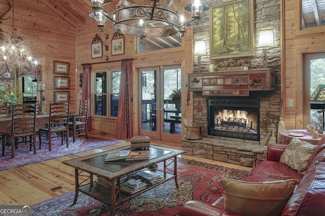 living area with wooden walls, an inviting chandelier, a fireplace, high vaulted ceiling, and wood finished floors