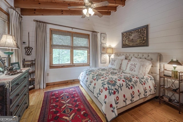 bedroom featuring wood walls, lofted ceiling with beams, and light wood-style flooring