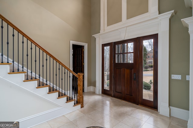 foyer entrance featuring baseboards, a towering ceiling, tile patterned floors, and stairway