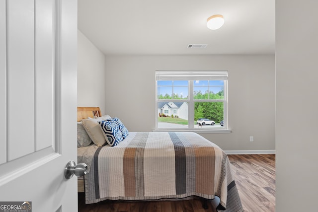 bedroom with baseboards, visible vents, and wood finished floors