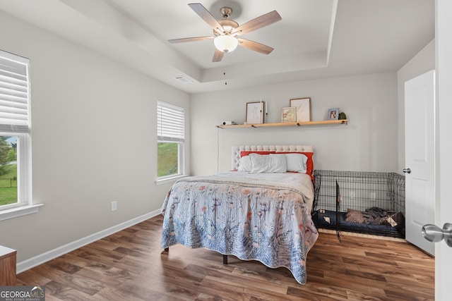bedroom with ceiling fan, a raised ceiling, baseboards, wood finished floors, and visible vents