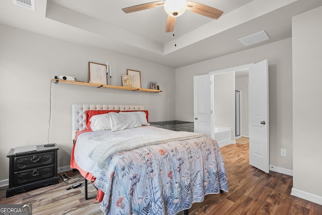 bedroom with baseboards, visible vents, wood finished floors, and a raised ceiling