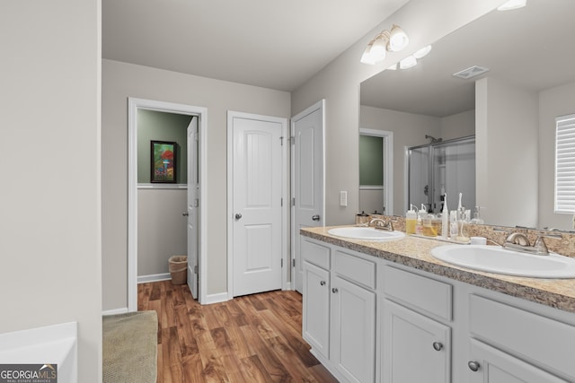 full bath with a sink, a stall shower, wood finished floors, and visible vents