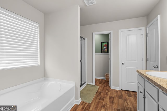 full bath with vanity, wood finished floors, visible vents, a garden tub, and a stall shower