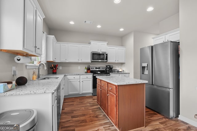 kitchen featuring light stone counters, a sink, dark wood finished floors, stainless steel appliances, and white cabinetry