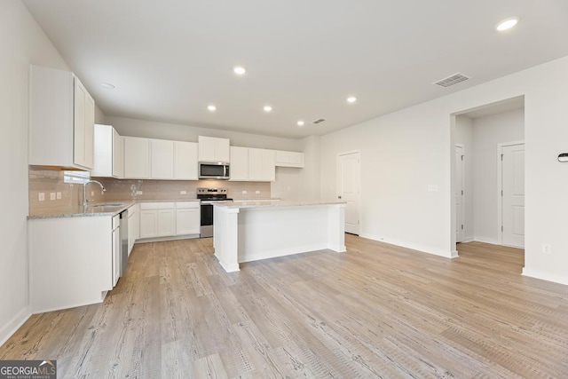 kitchen with decorative backsplash, appliances with stainless steel finishes, a center island, a sink, and white cabinets