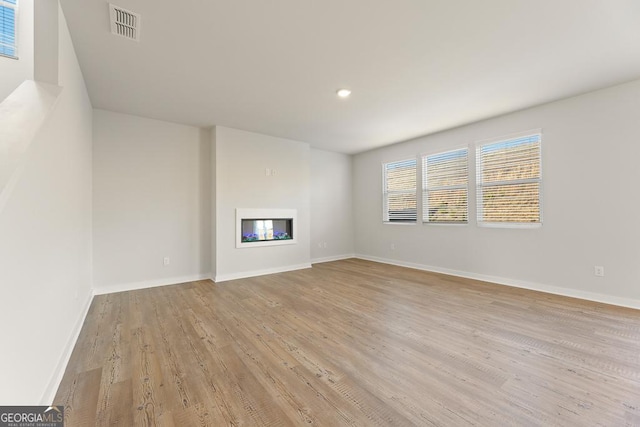 unfurnished living room with a glass covered fireplace, baseboards, light wood finished floors, and visible vents