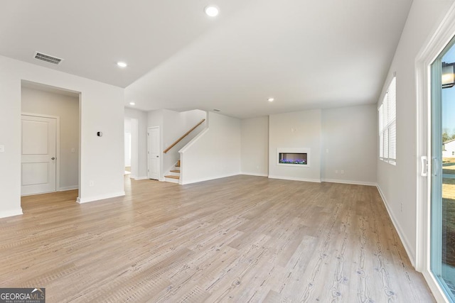 unfurnished living room featuring light wood finished floors, a glass covered fireplace, stairs, recessed lighting, and visible vents