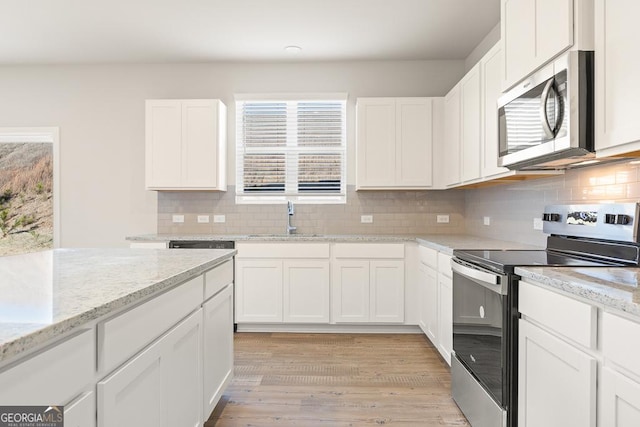 kitchen with decorative backsplash, white cabinetry, a sink, light wood-style flooring, and appliances with stainless steel finishes
