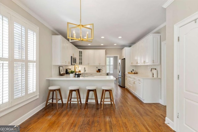 12892 Waterside Dr, Milton, GA 30004 - kitchen with crown molding, a notable chandelier, stainless steel appliances, a peninsula, and decorative backsplash