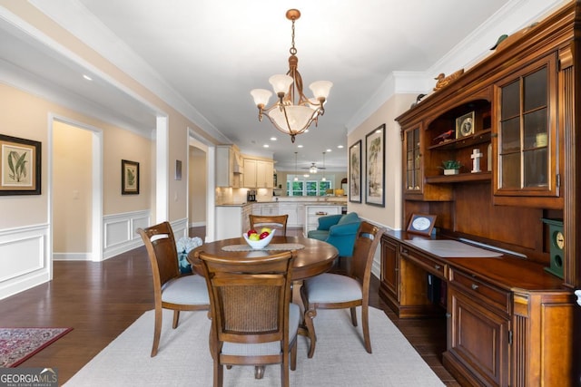 dining space with an inviting chandelier, crown molding, a wainscoted wall, and dark wood-style floors