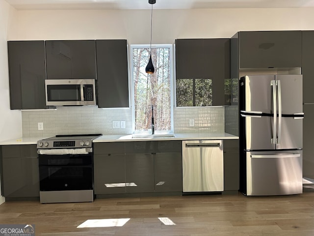 kitchen with appliances with stainless steel finishes, a sink, light countertops, gray cabinets, and backsplash