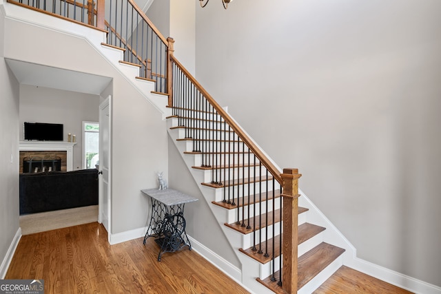 68 Timber Creek Estates Dr, Sharpsburg, GA 30277 - stairs featuring baseboards, a stone fireplace, wood finished floors, and a towering ceiling