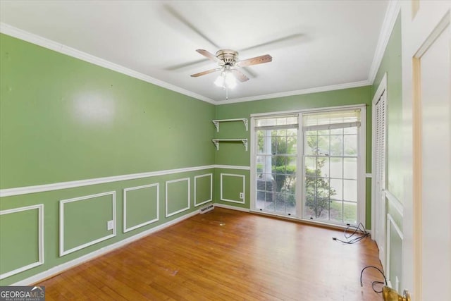 spare room with ceiling fan, a decorative wall, wood finished floors, ornamental molding, and wainscoting