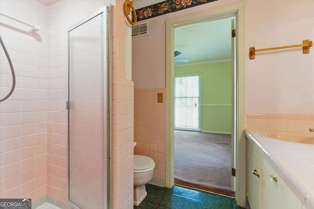 bathroom with tile walls, a stall shower, vanity, toilet, and a wainscoted wall