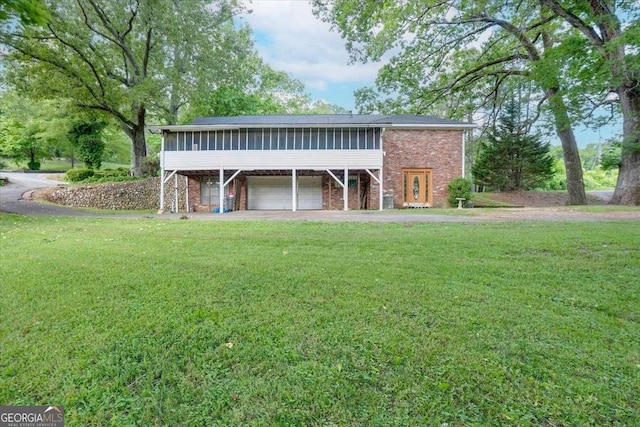 back of property with a sunroom, a garage, a yard, brick siding, and driveway