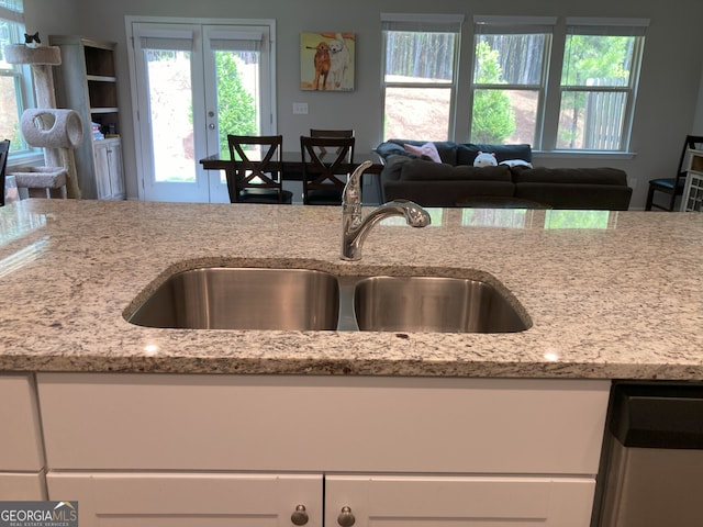 kitchen with white cabinets, light stone counters, a sink, french doors, and open floor plan