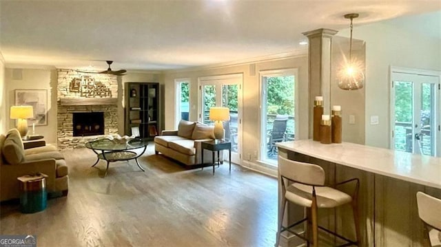 living room with ornamental molding, a stone fireplace, a ceiling fan, and wood finished floors