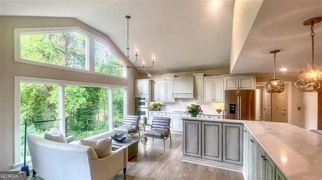kitchen featuring hanging light fixtures, high vaulted ceiling, stainless steel appliances, wood finished floors, and custom range hood