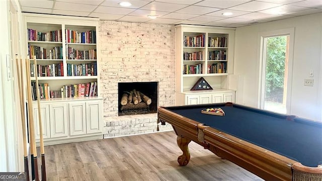 game room with a brick fireplace, built in shelves, a paneled ceiling, pool table, and wood finished floors