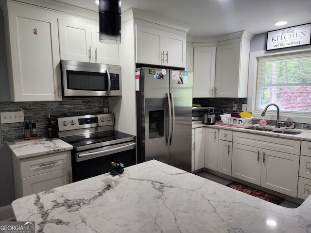kitchen with decorative backsplash, white cabinetry, light stone counters, a sink, and appliances with stainless steel finishes