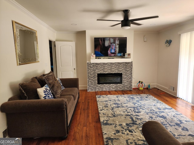 living area with ornamental molding, wood finished floors, a fireplace, baseboards, and a ceiling fan