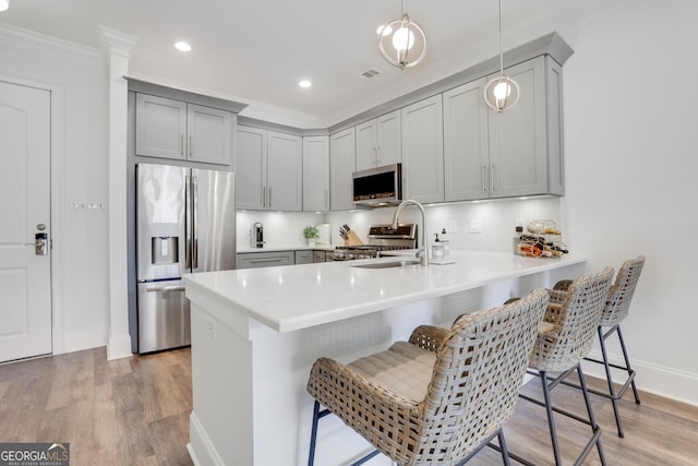 kitchen featuring appliances with stainless steel finishes, gray cabinetry, a peninsula, a kitchen breakfast bar, and crown molding