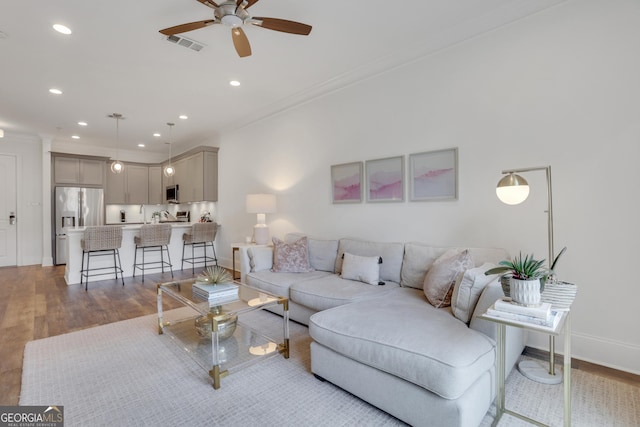 living area featuring ornamental molding, a ceiling fan, wood finished floors, baseboards, and recessed lighting
