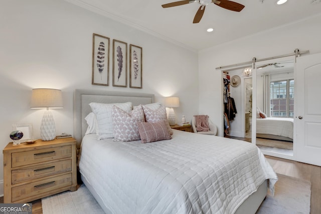 bedroom with crown molding, a walk in closet, recessed lighting, wood finished floors, and a closet